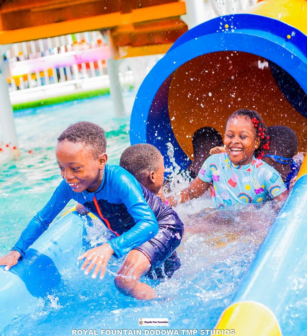 Three children laughing as they splash out of a tube slide