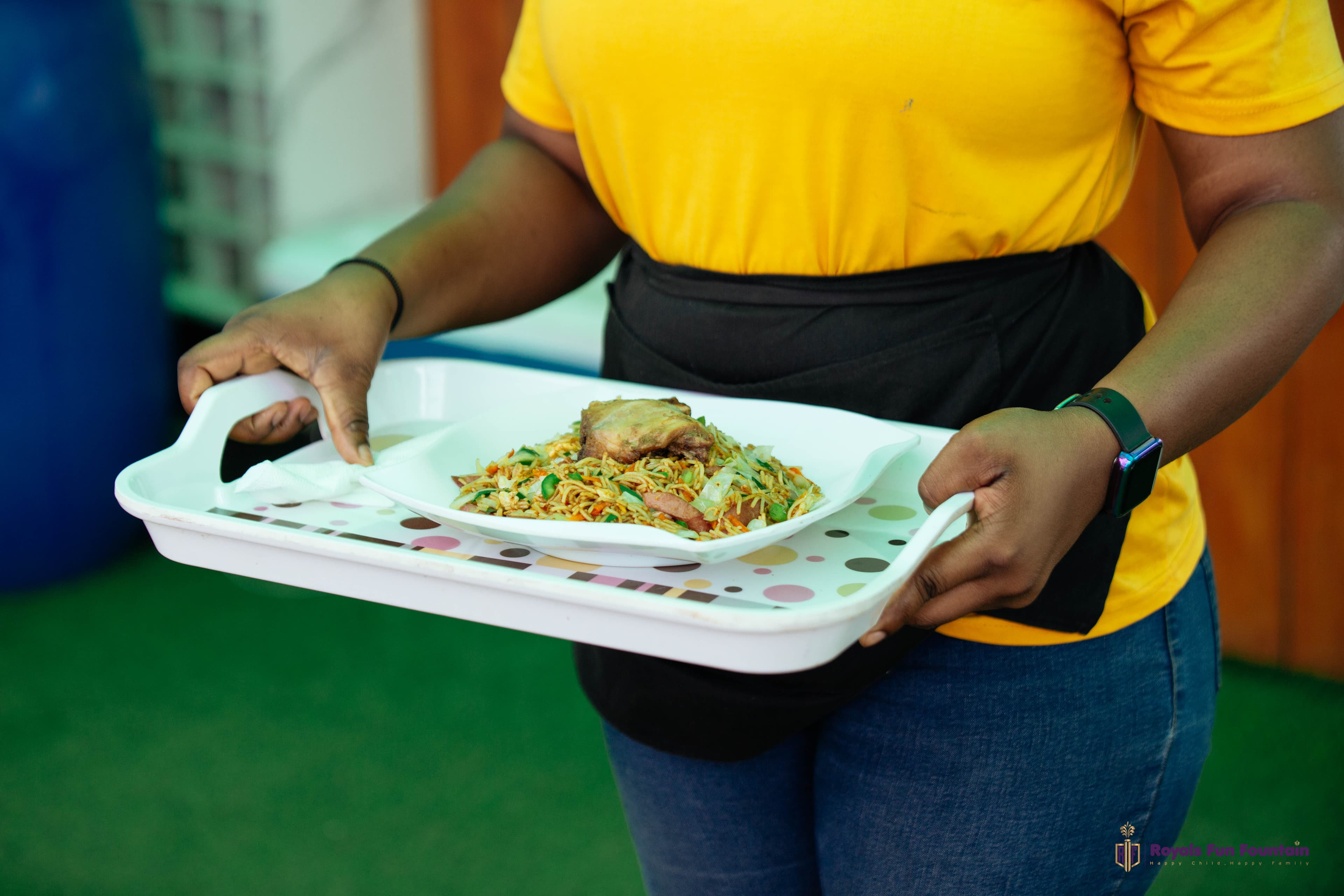 A server carrying a plate of noodles and chicken on a tray